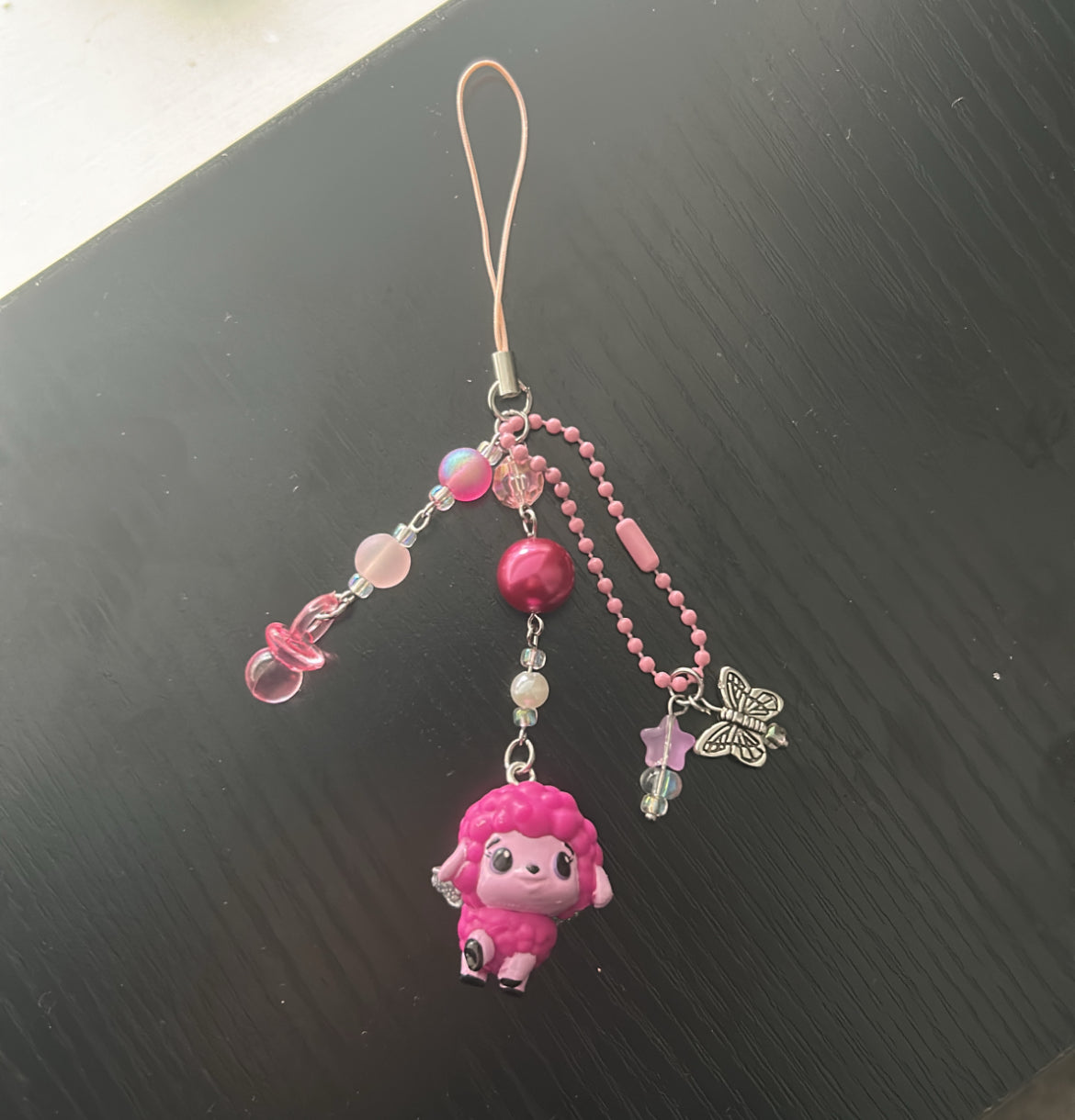Pink character phone charm with beads on a black surface