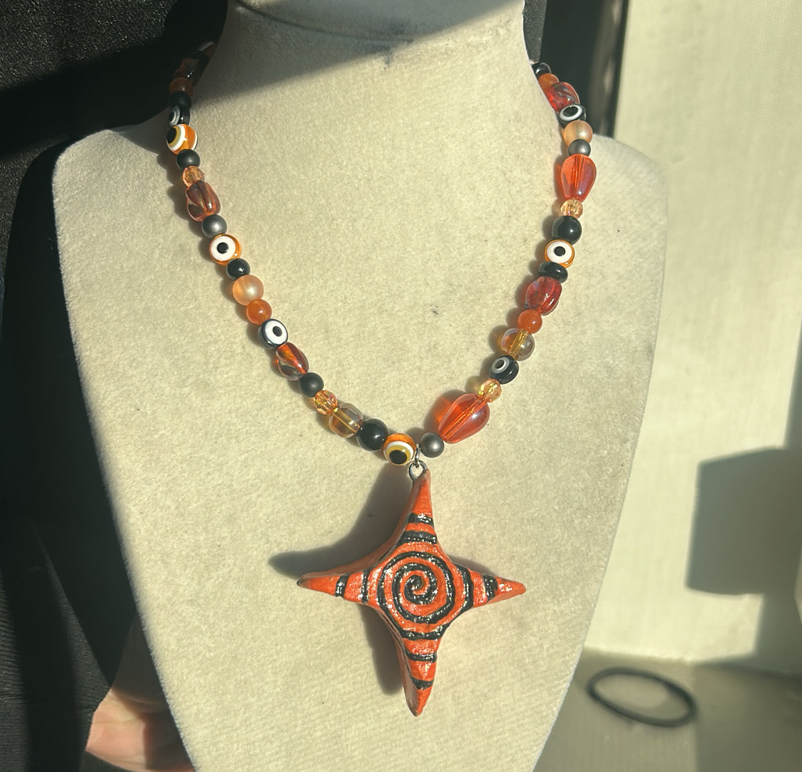Orange beaded Necklace with a star-shaped clay pendant on a mannequin bust