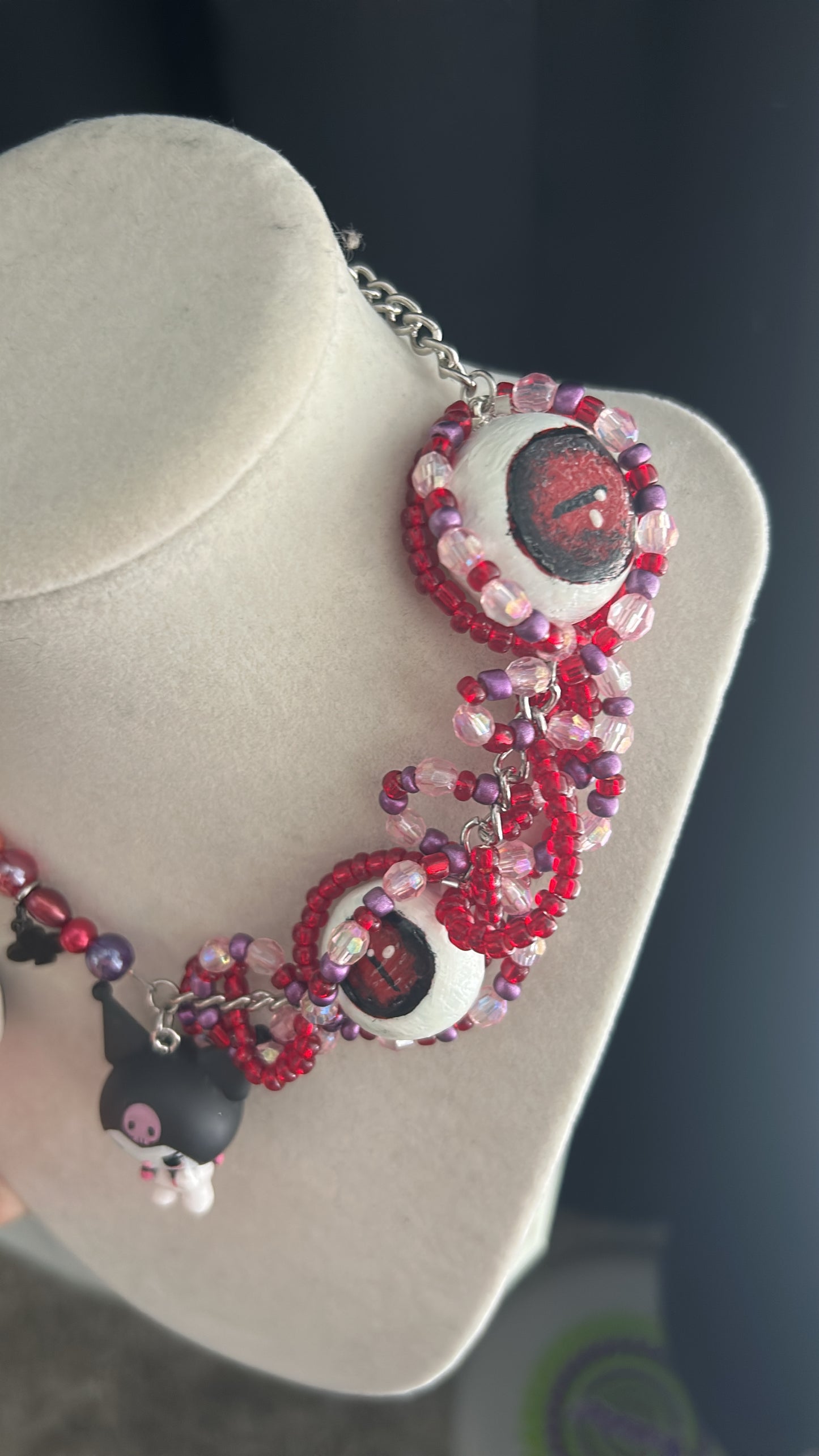 Beaded necklace with black and white charms on a gray stand against a dark background